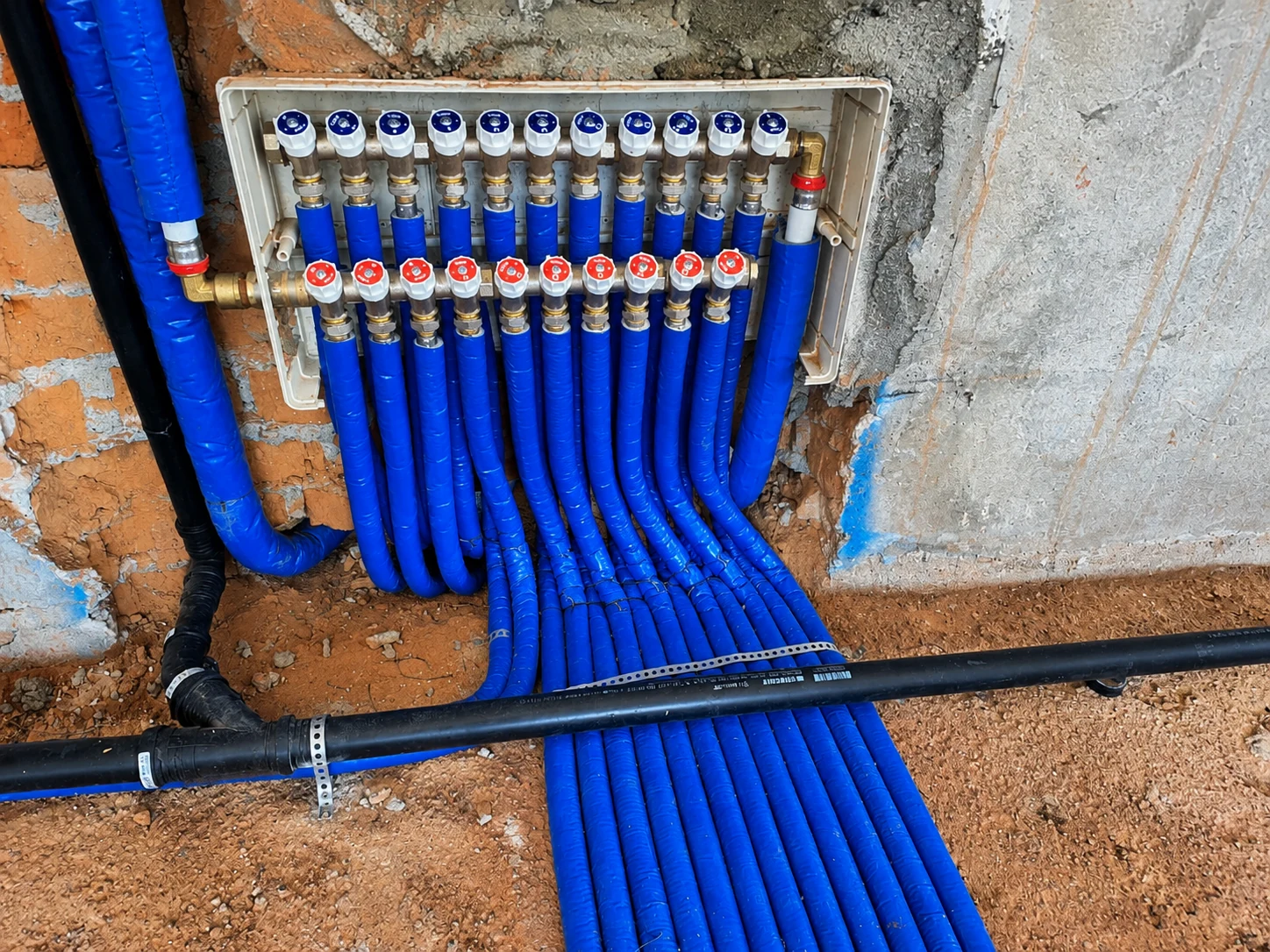 Collettore idraulico con tubazioni blu coibentate ordinate installato in una parete di cantiere